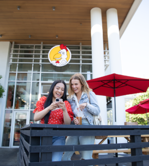 Two girls looking at a phone on DownLow Chicken's patio.